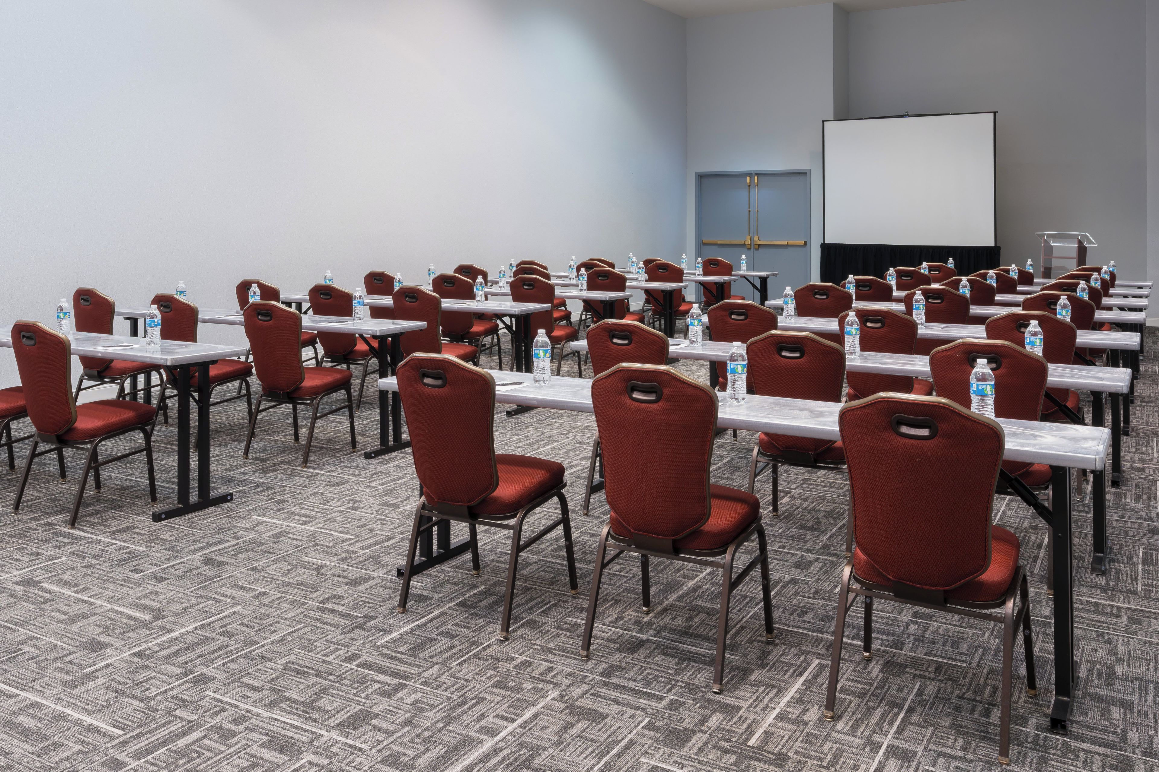 A conference room with rows of tables and chairs, equipped with water bottles.
