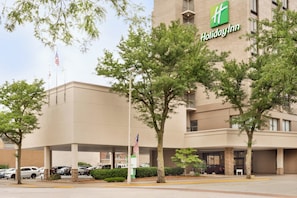Un hotel Holiday Inn con estacionamiento, bandera y árboles.