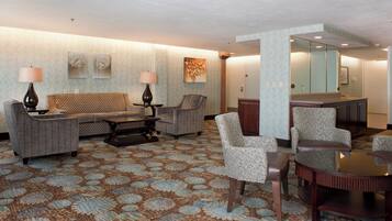 Un vestíbulo de hotel con alfombra estampada, un sofá, sillones, una mesa de centro y un espejo.
