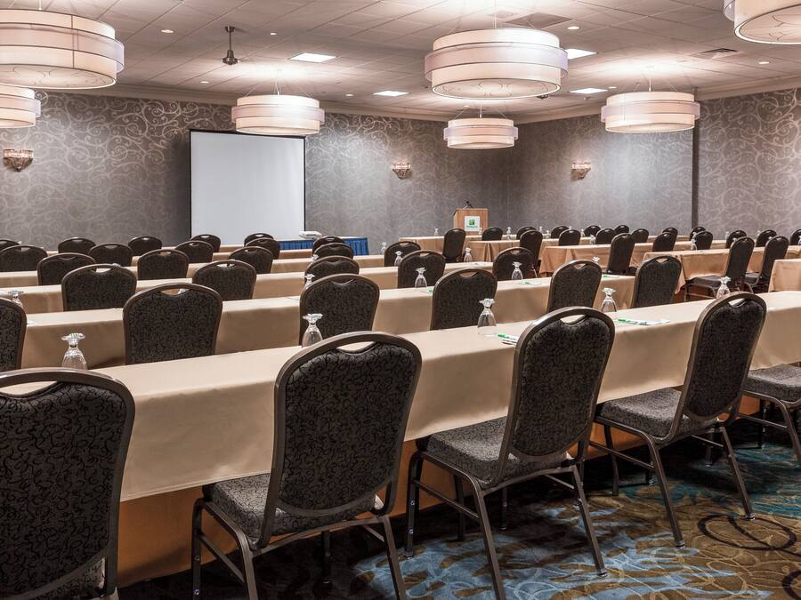 A conference room with rows of tables and chairs, a podium, and a projector screen.