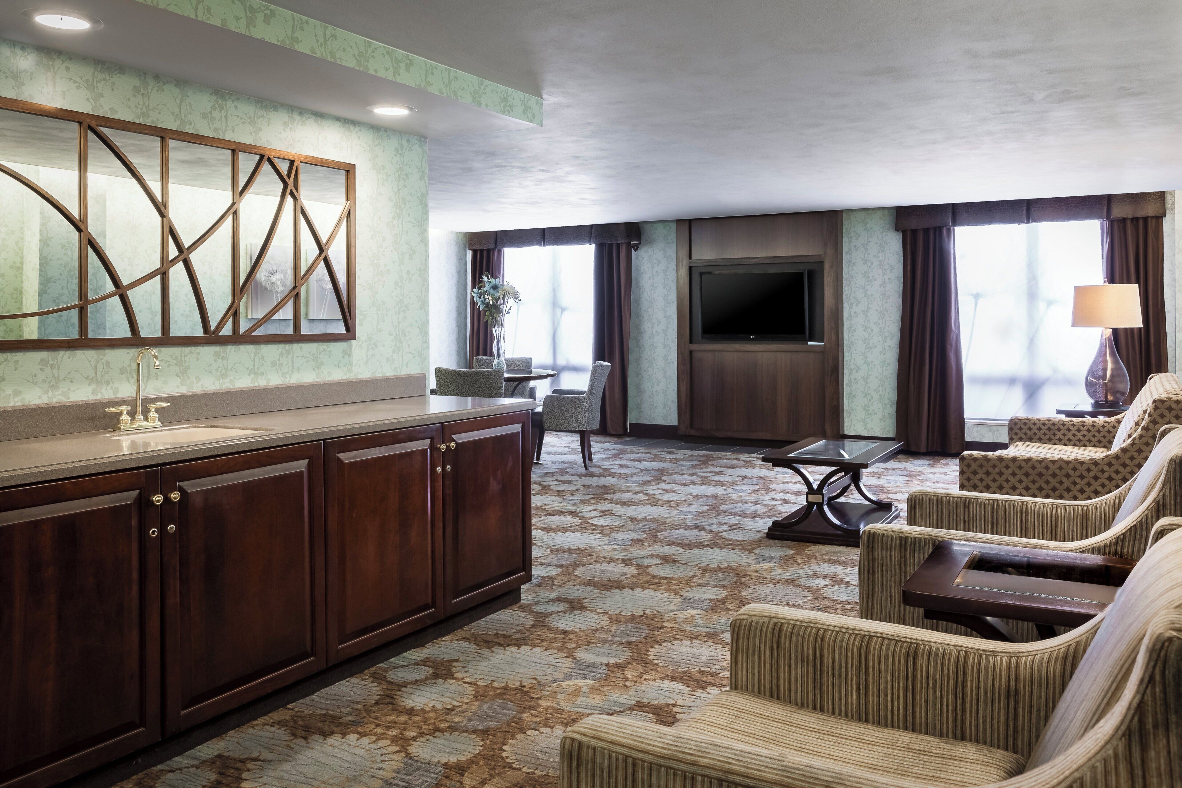 A hotel room with a wooden cabinet, a flat-screen TV, a sofa, and a patterned carpet.