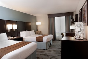Habitación de hotel con dos camas, un escritorio, una lámpara y vistas al exterior.
