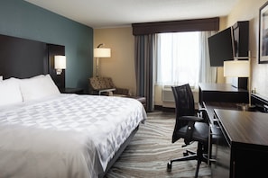 Une chambre d’hôtel avec un grand lit, un bureau, une chaise, une télévision et une fenêtre avec des rideaux.