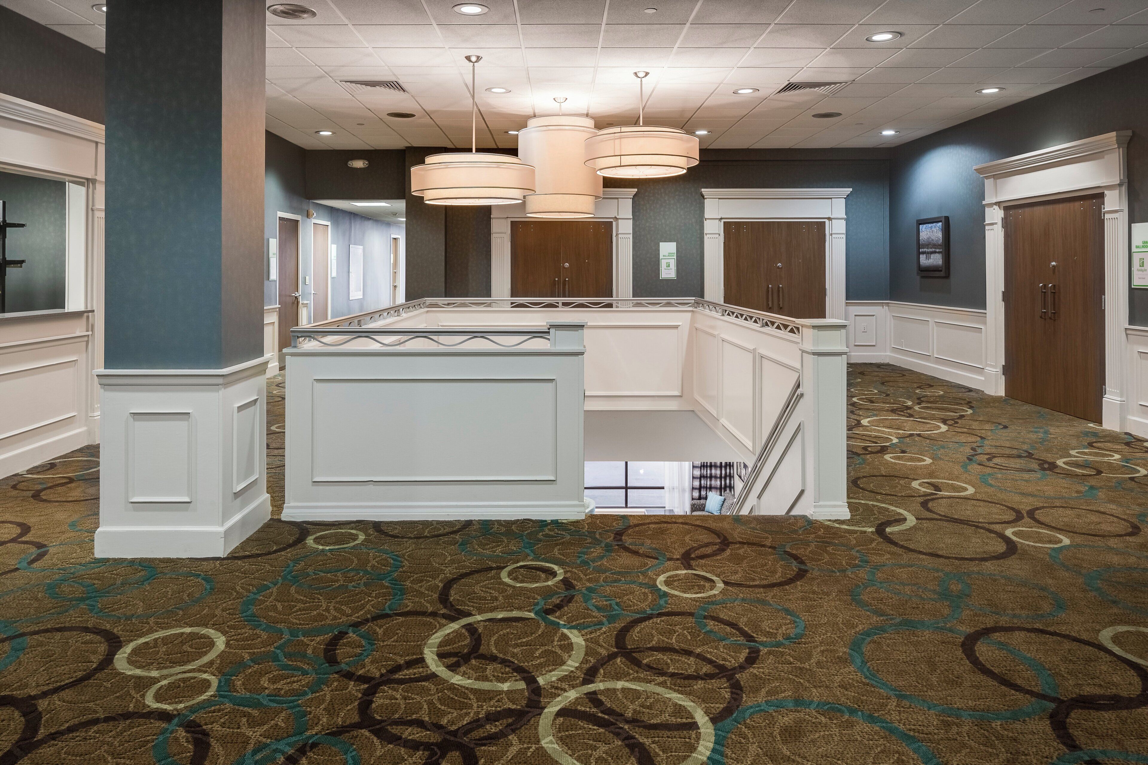 A hotel lobby with a central island, a patterned carpet, and a ceiling with recessed lighting.