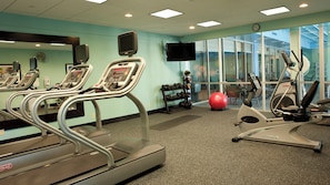 Un gimnasio con cintas de correr, una bicicleta estática y una pelota roja de ejercicios.