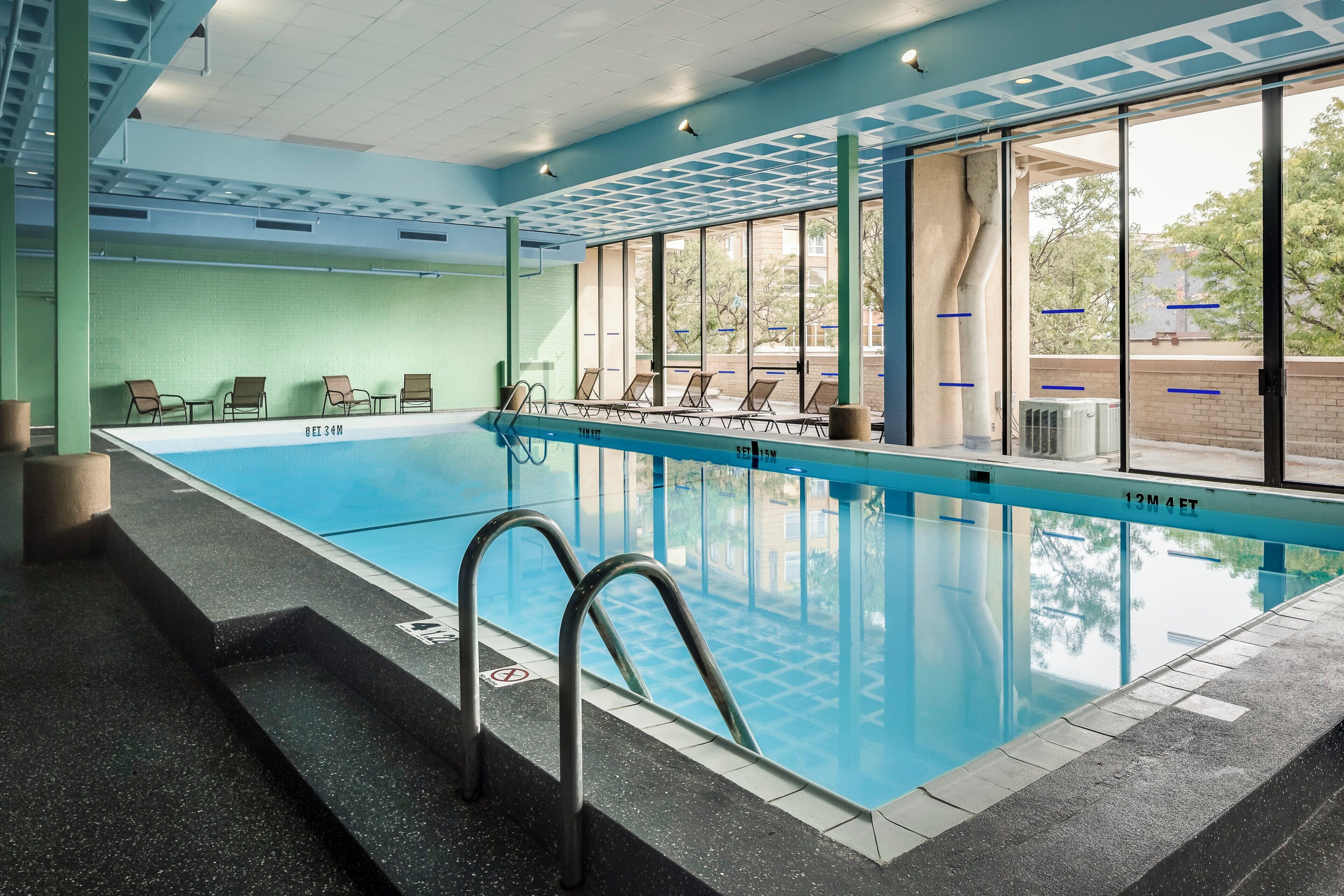 A swimming pool with clear water, surrounded by lounge chairs and a glass wall.