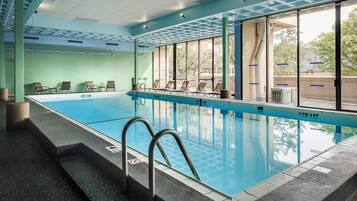 A swimming pool with clear water, surrounded by lounge chairs and a glass wall.