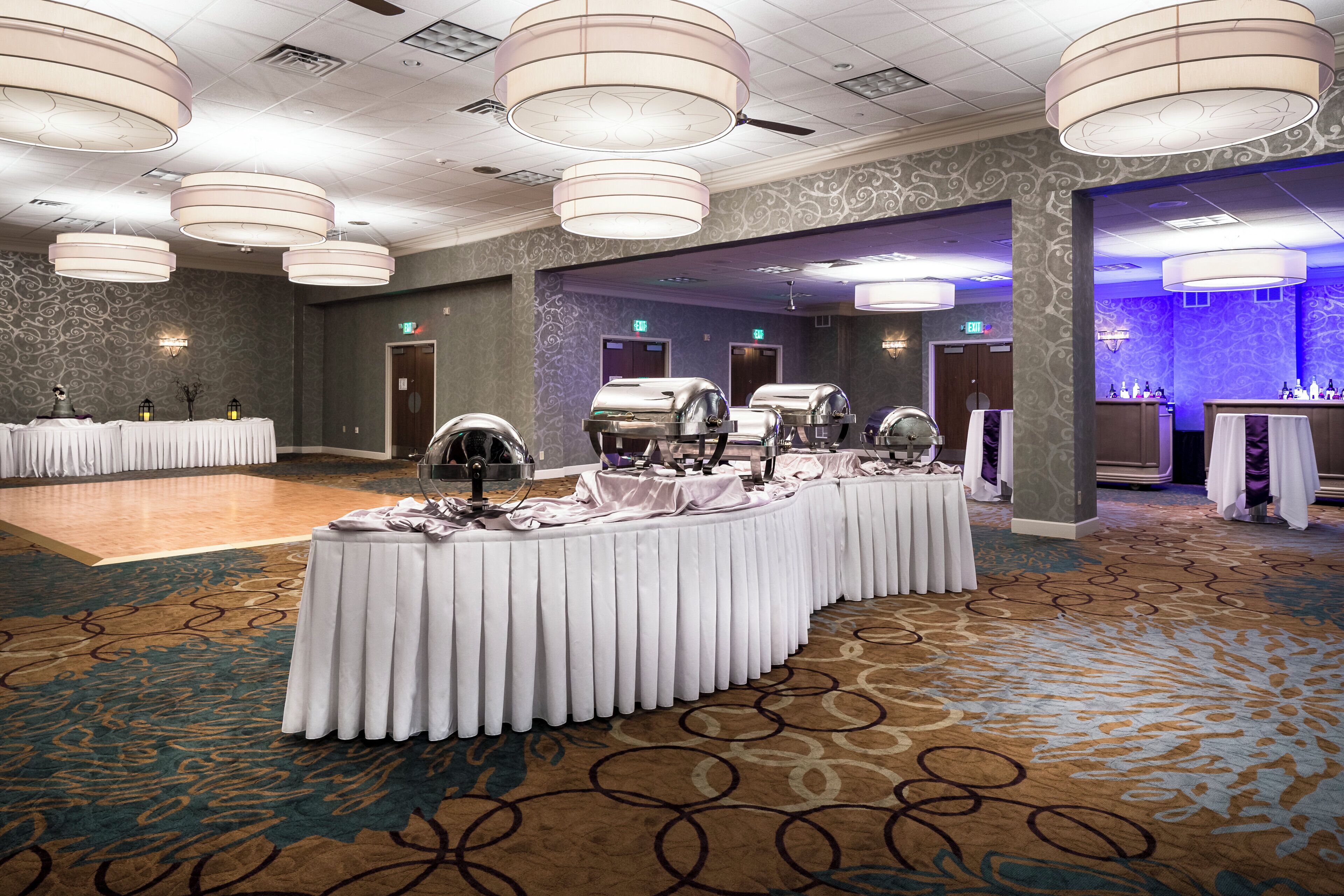 A banquet hall with a long table covered in white tablecloths, equipped with a grill station, and surrounded by high ceiling chandeliers.