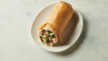 A burrito wrapped in paper on a white plate.