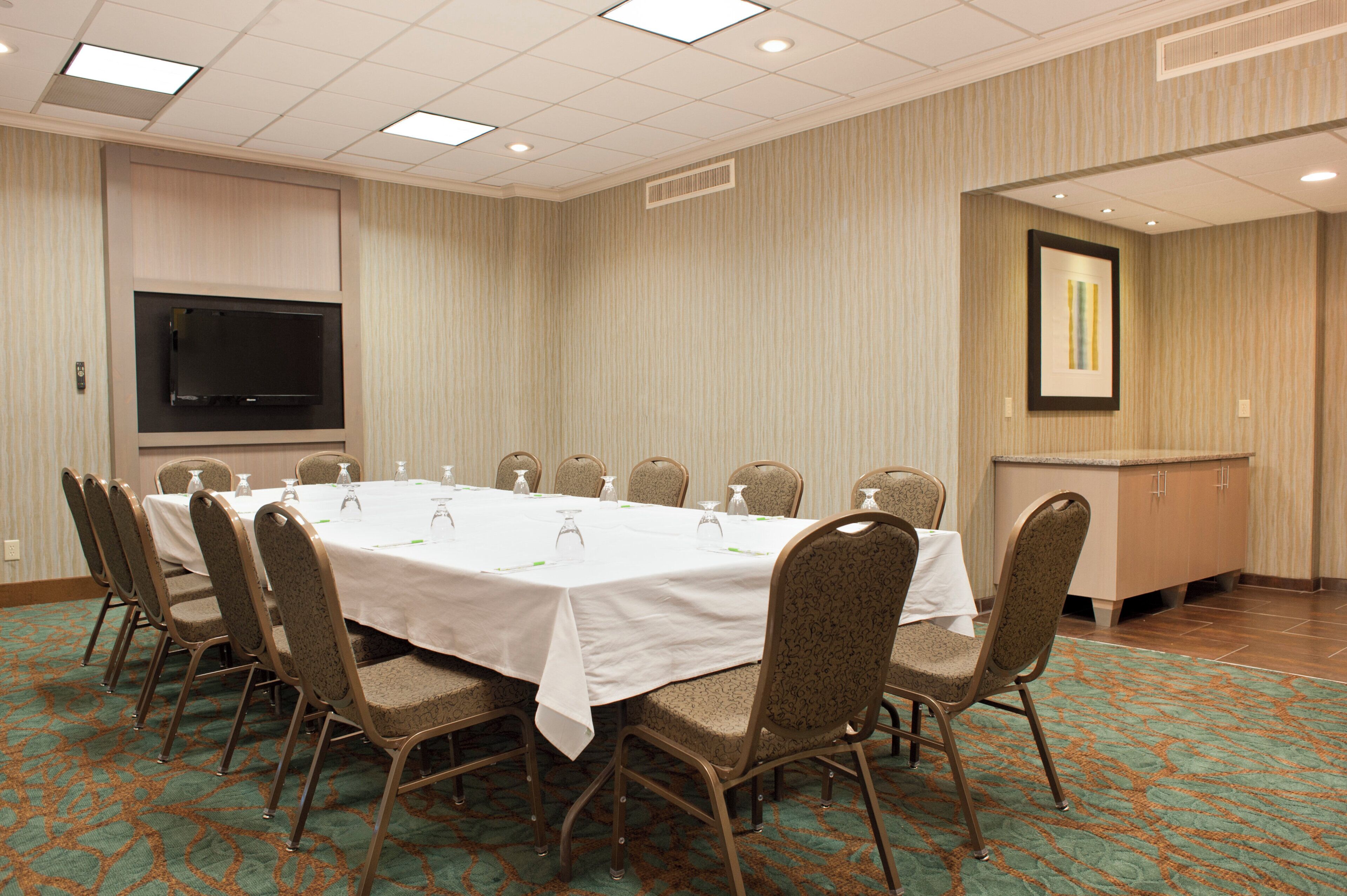 A conference room with a long table, chairs, a flat-screen TV, and a framed picture on the wall.