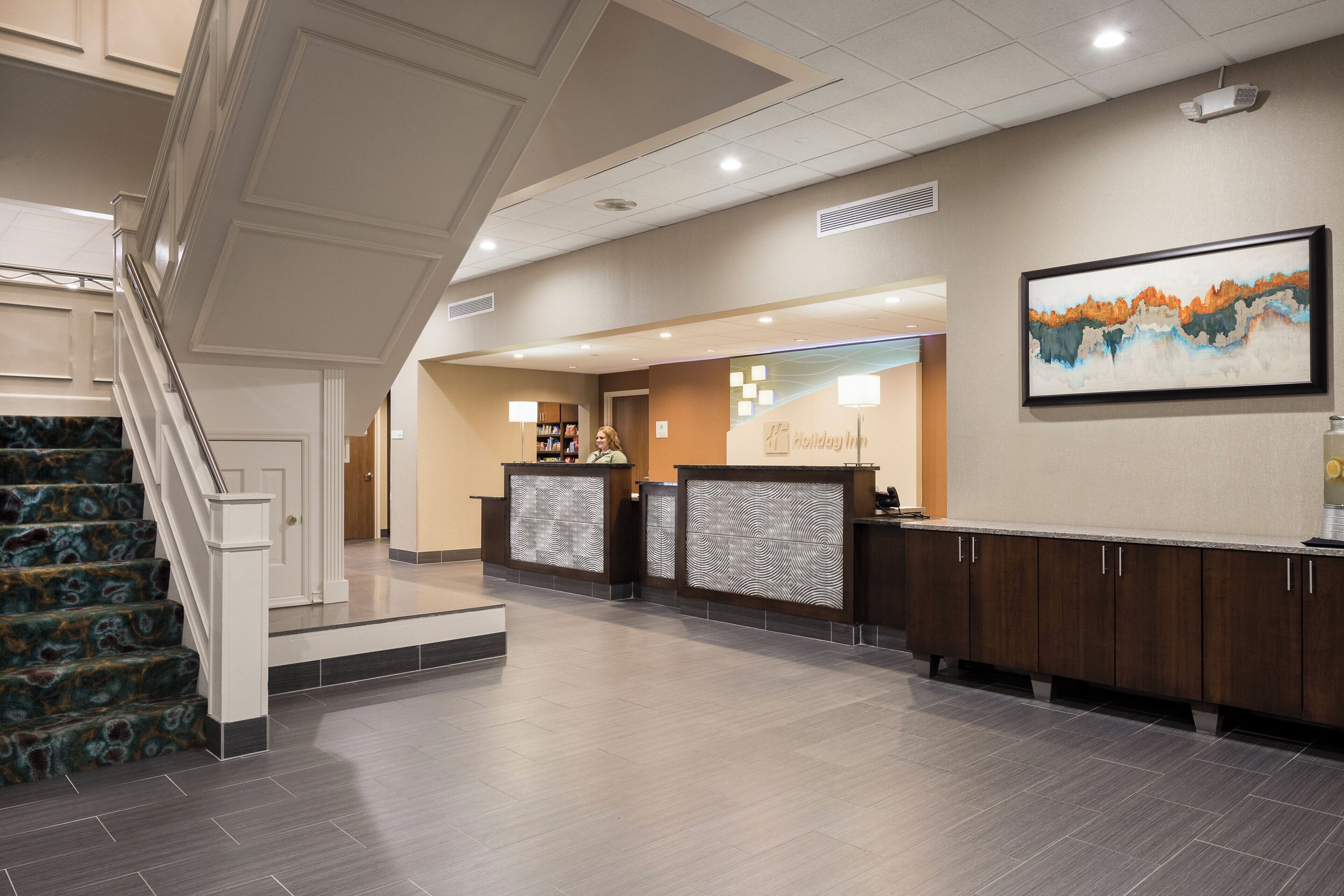 A hotel reception area with a staircase, reception desk, and a painting on the wall.