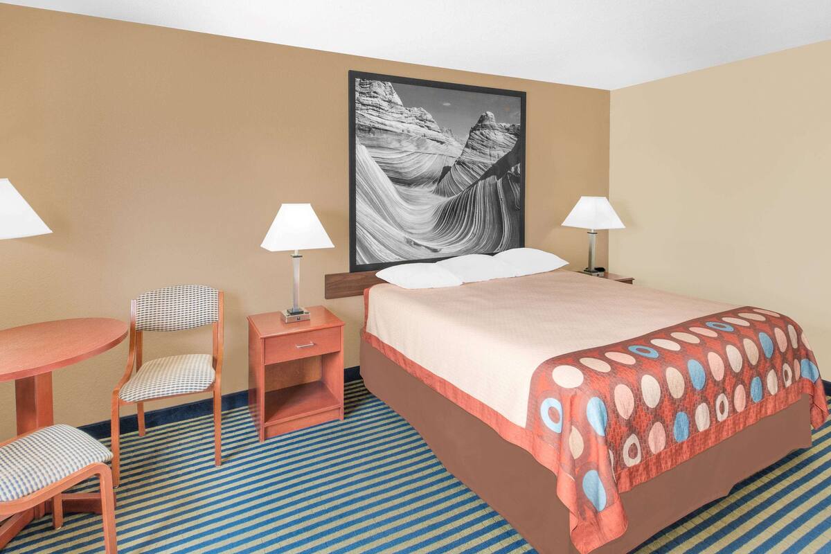 Een hotelkamer met een bed, twee nachtkastjes met lampen, een stoel en een groot schilderij aan de muur.