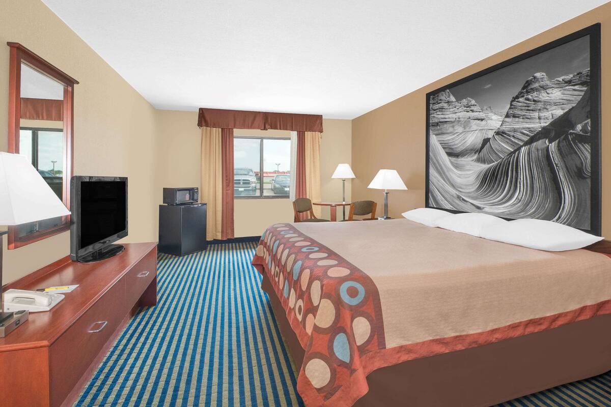 Hotelkamer met een bed, een bureau met een televisie, twee lampen en een groot schilderij van een canyon.