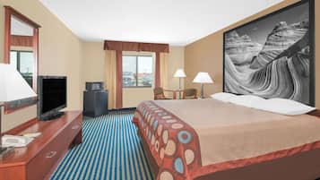 A hotel room with a bed, a desk with a television, two lamps, and a large painting of a canyon.