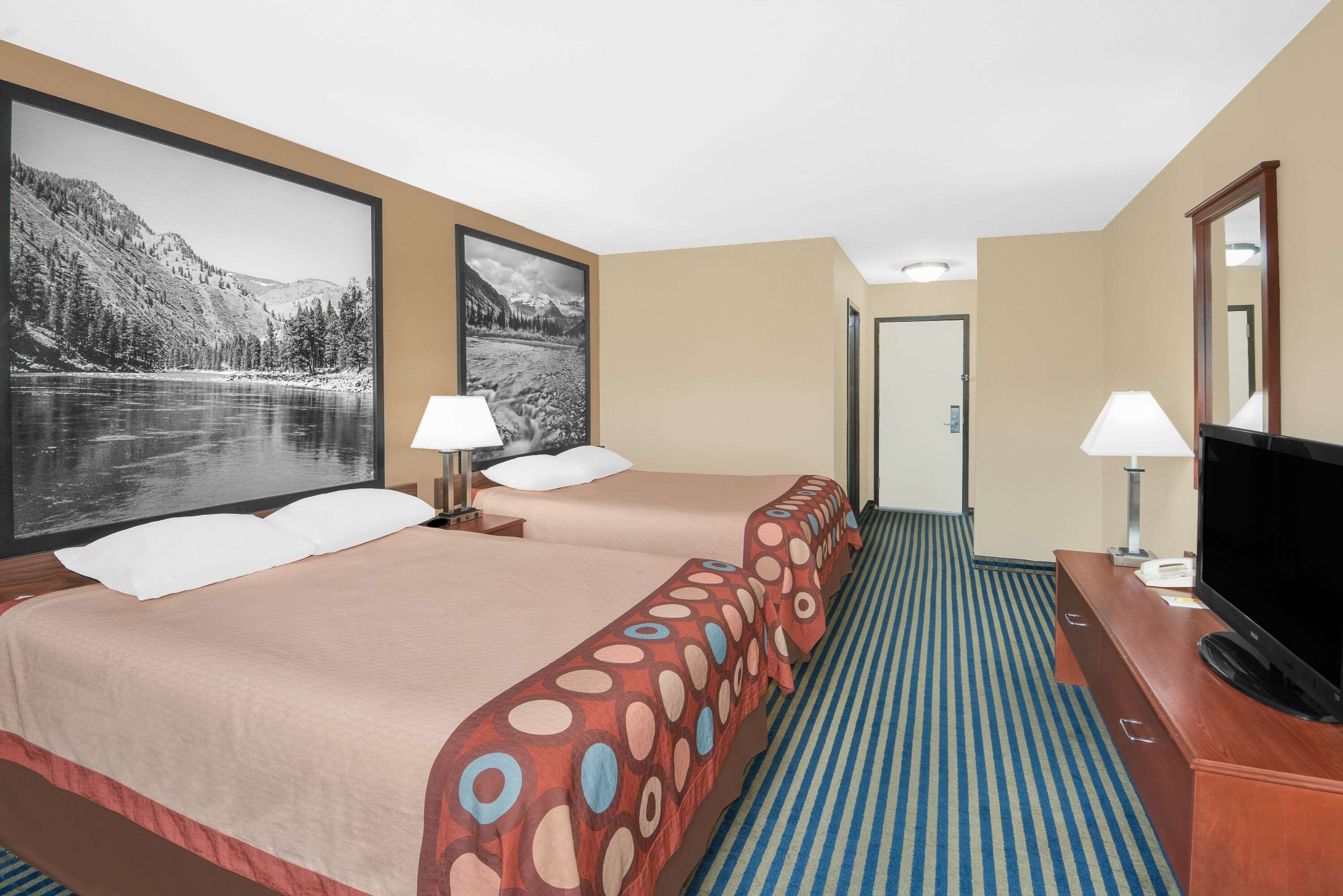 Une chambre d’hôtel avec deux lits, une télévision et un grand tableau représentant un paysage de montagne.