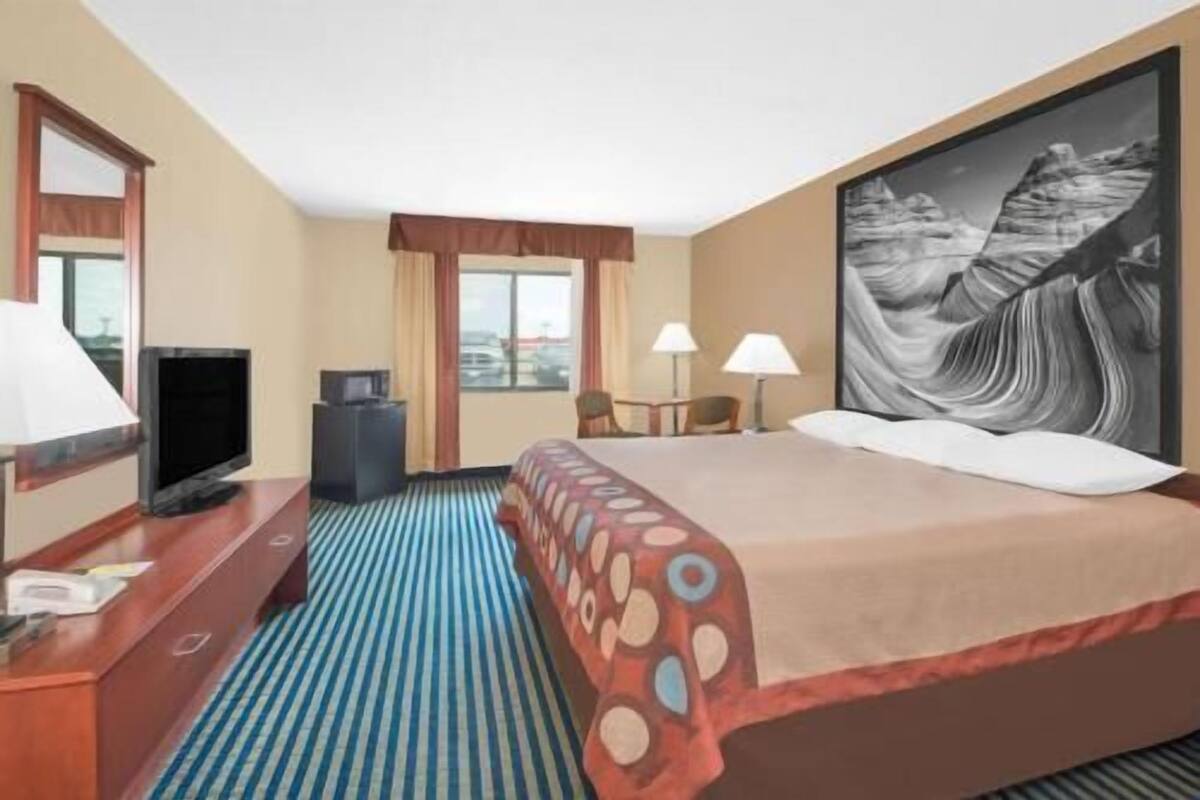 Een hotelkamer met een bed, een bureau met een televisie, een stoel, een lamp en een schilderij aan de muur.