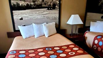 A hotel room with a large bed, two pillows, a nightstand with a lamp, and a large window with a black and white landscape view.