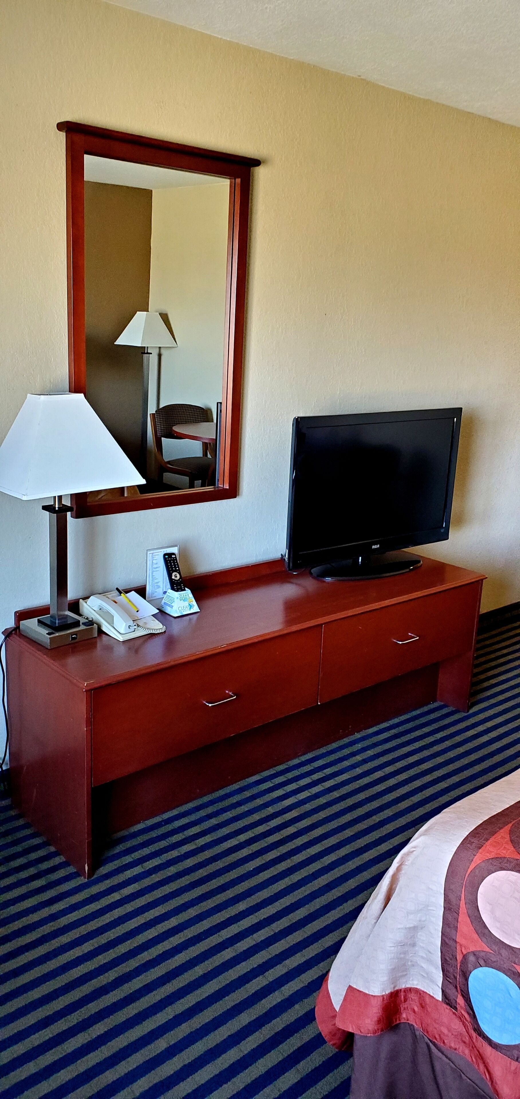 A hotel room with a wooden desk, a television, a lamp, and a telephone.