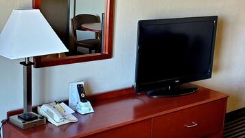 Una habitación de hotel con un escritorio de madera, un televisor, una lámpara y un teléfono.