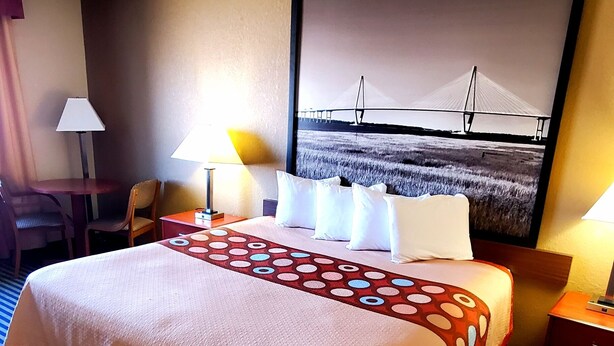 Hotelkamer met een groot bed, twee bedlampen, een stoel, een bureau en een aan de muur bevestigde televisie waarop een brug te zien is.