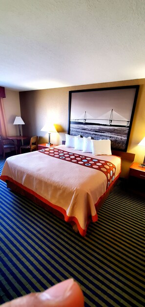Hotelkamer met een groot bed, twee bedlampen, een stoel, een bureau en een aan de muur bevestigde televisie waarop een brug te zien is.