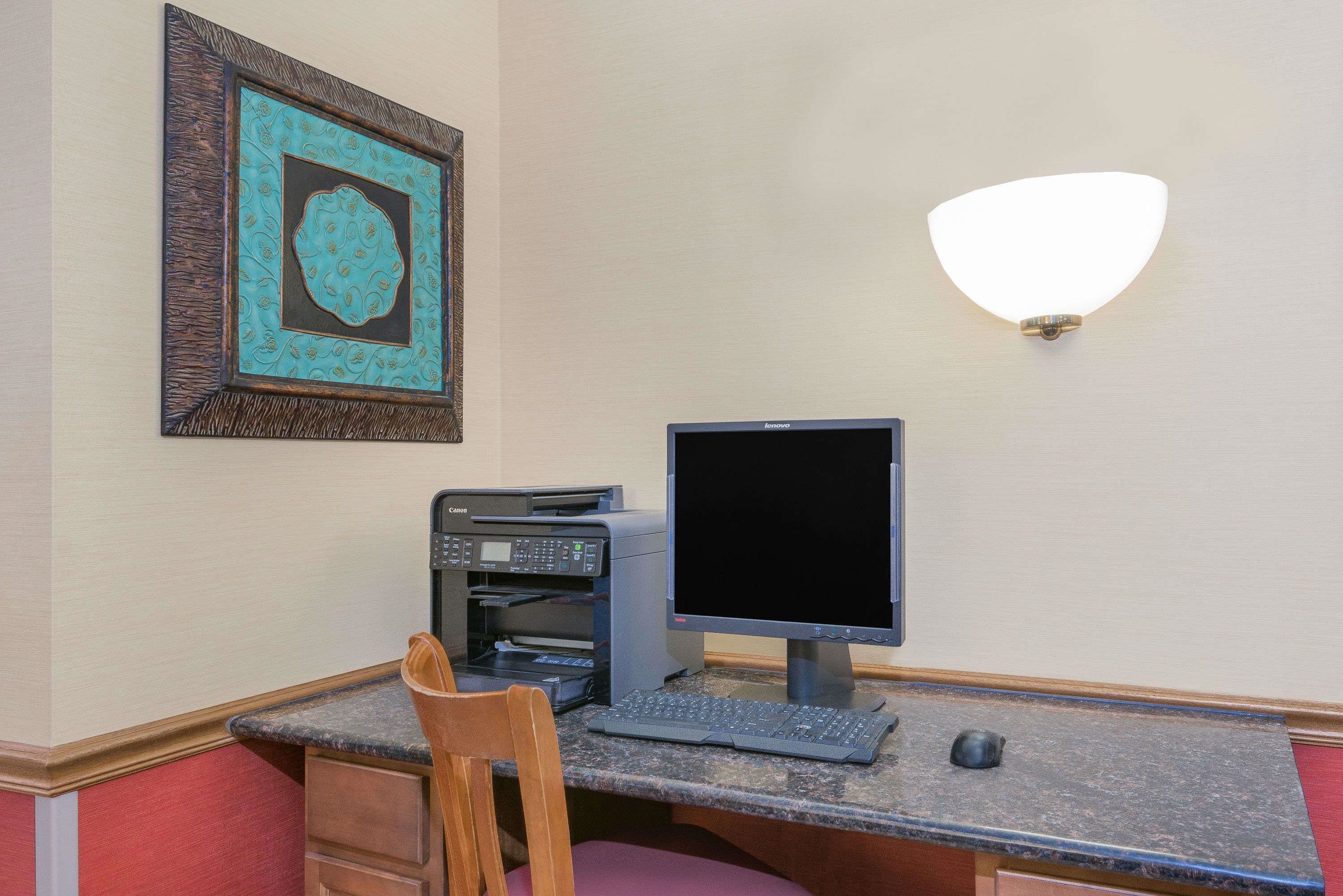 A workspace with a desktop computer, printer, and a framed artwork on the wall.