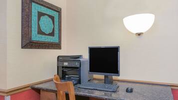 A workspace with a desktop computer, printer, and a framed artwork on the wall.