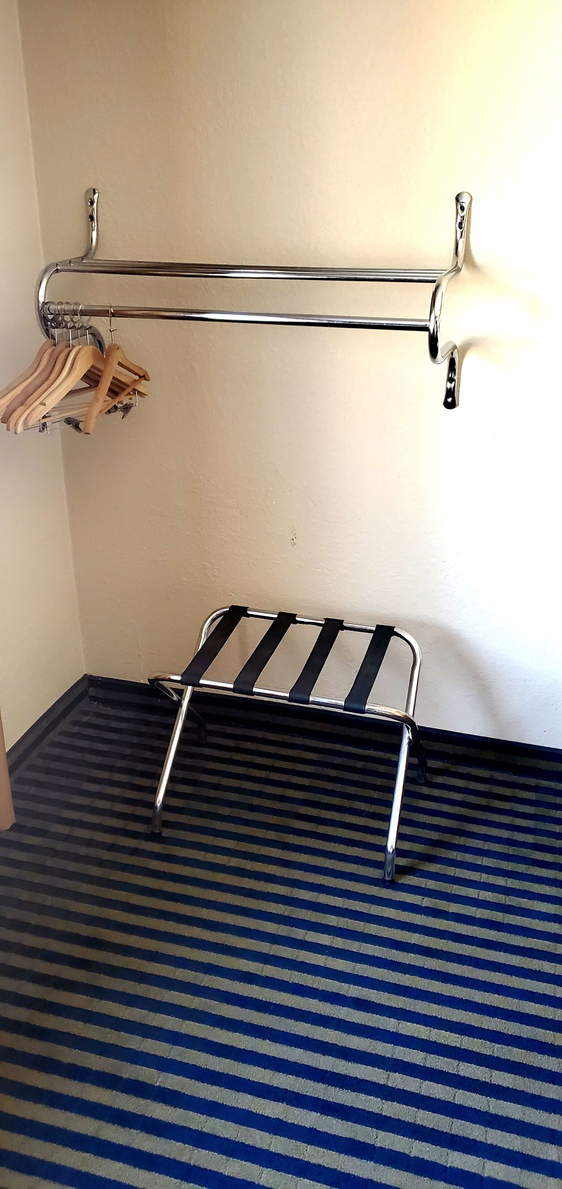 A metal rack with wooden hangers, a metal stool, and a striped carpet in a room.