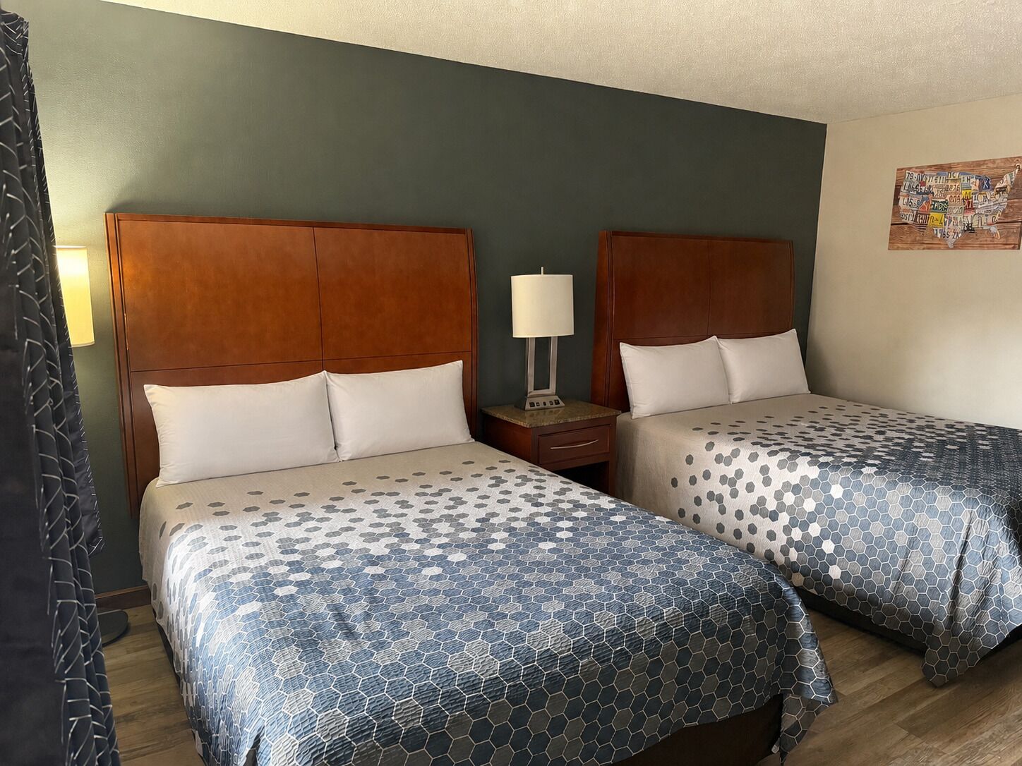 A hotel room with two beds, wooden headboards, and a nightstand with a lamp.