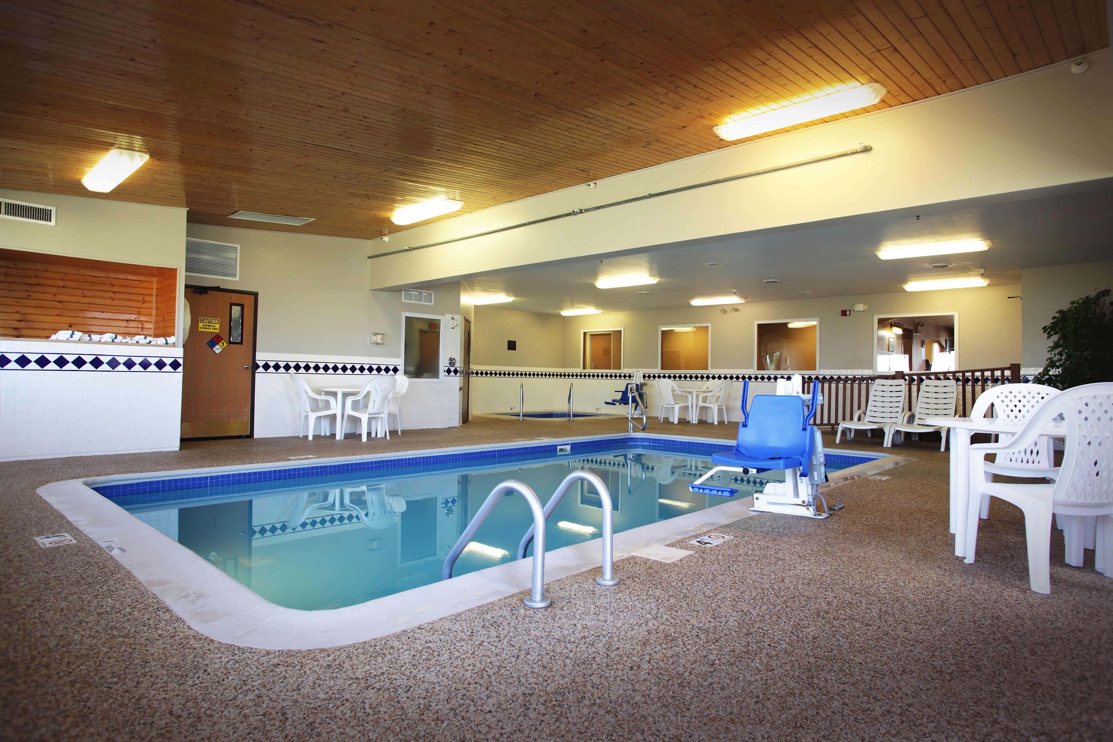 Una piscina interior con borde de azulejos, una silla azul y otras blancas alrededor del borde.