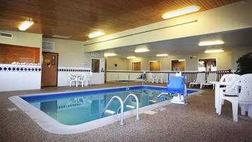 Una piscina interior con borde de azulejos, una silla azul y otras blancas alrededor del borde.