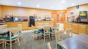Un restaurant amb mobiliari de fusta, un sòl de rajoles i una zona de cuina amb electrodomèstics.