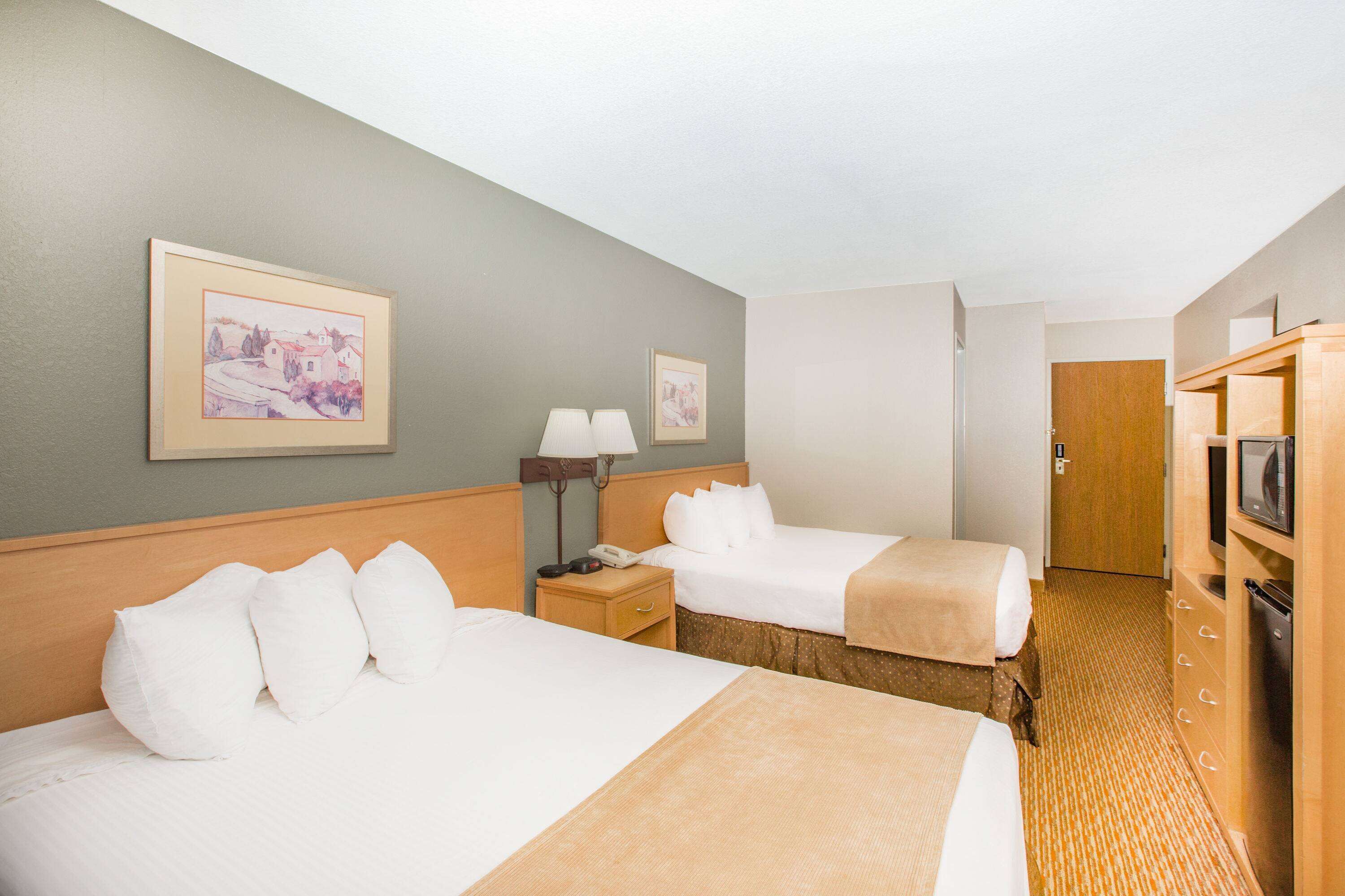 Een hotelkamer met twee bedden, een houten hoofdbord, een nachtkastje met een lamp, een houten kledingkast en een lijst met een afbeelding aan de muur.