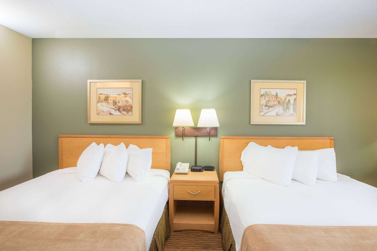 Una habitació d'hotel amb dos llits, una tauleta de nit amb una làmpada i dues fotografies encadrades a la paret.