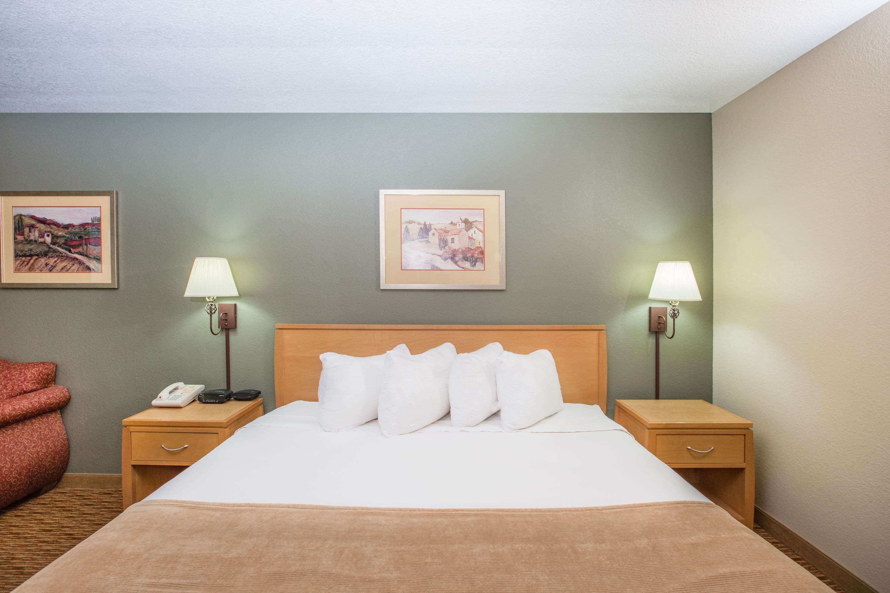 A hotel room with a large bed, two bedside tables, a lamp on each table, and two framed pictures on the wall.