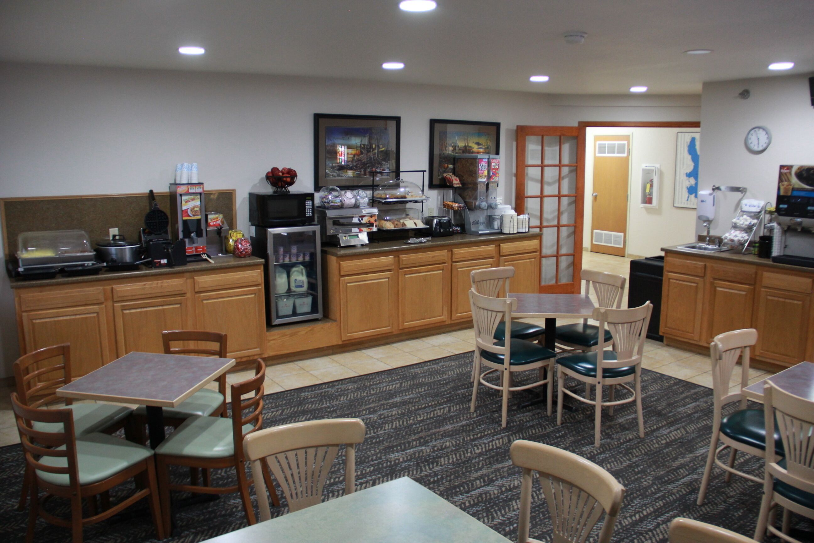 A hotel kitchen with wooden cabinets, a coffee station, and a seating area with tables and chairs.