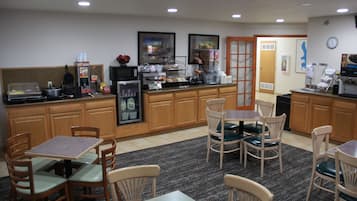 A hotel kitchen with wooden cabinets, a coffee station, and a seating area with tables and chairs.