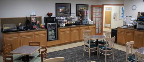 A hotel kitchen with wooden cabinets, a coffee station, and a seating area with tables and chairs.