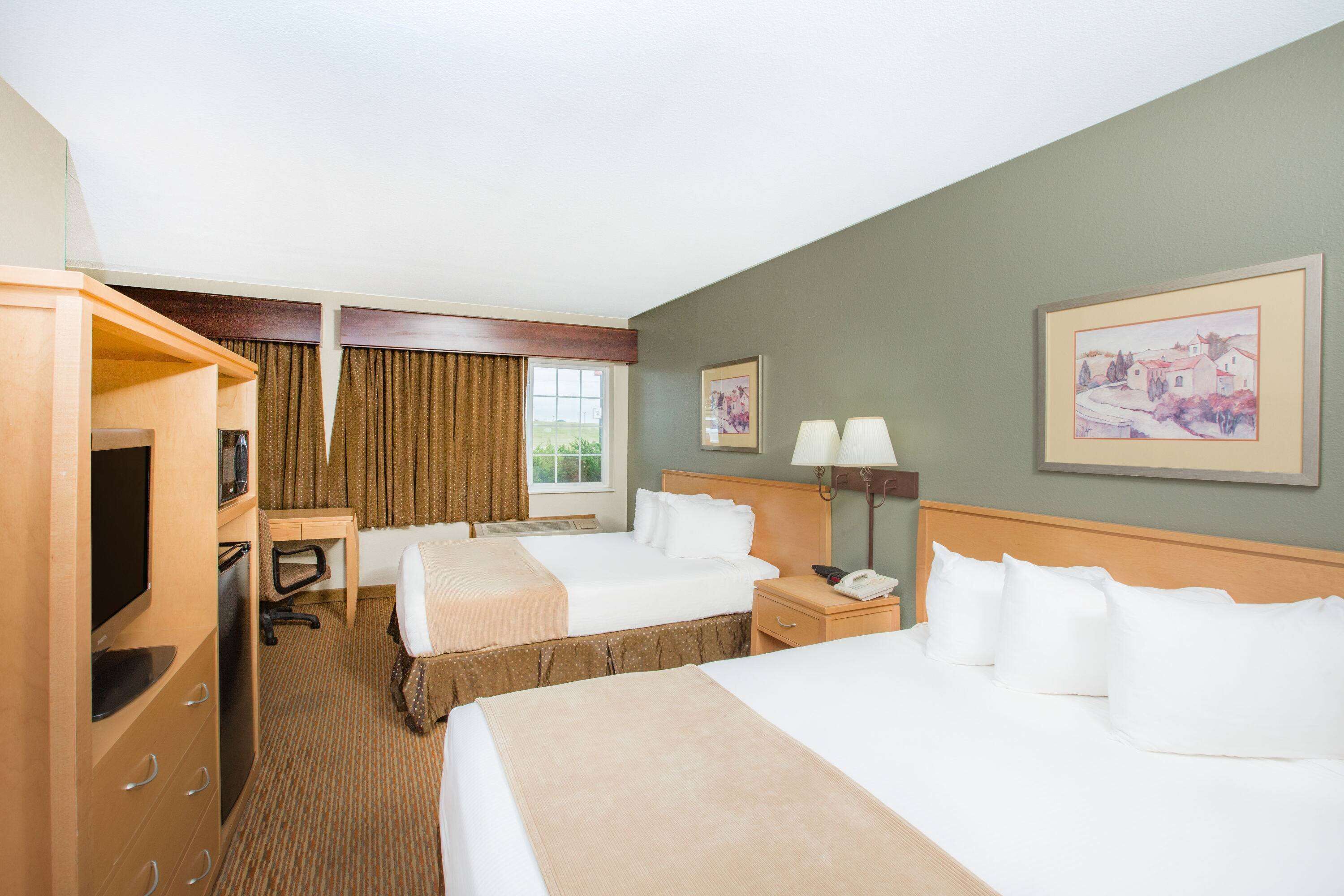 A hotel room with two beds, a desk, a TV, and a telephone.