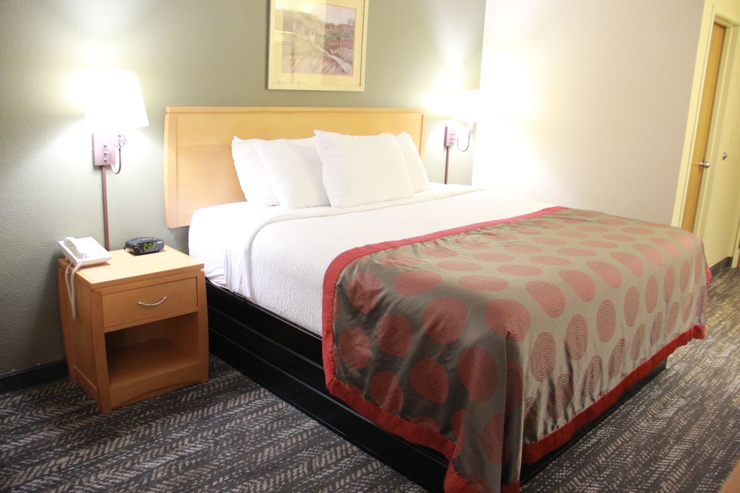 A hotel room with a bed, a nightstand, a lamp, and a painting on the wall.