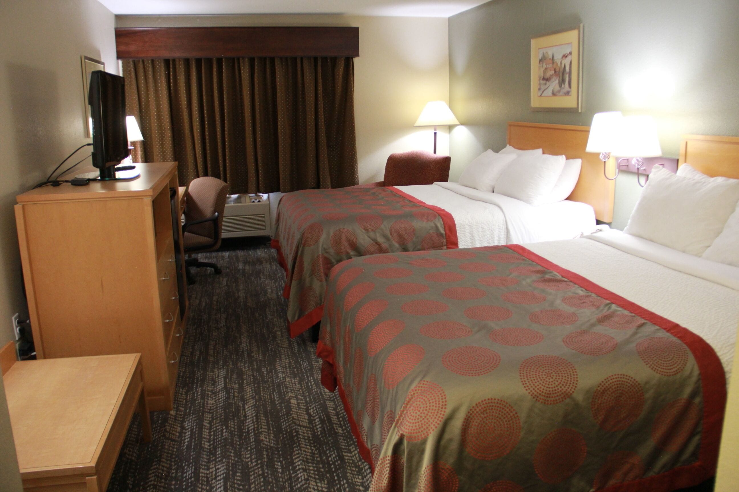 A hotel room with two beds, a desk with a computer, a chair, and a small table.