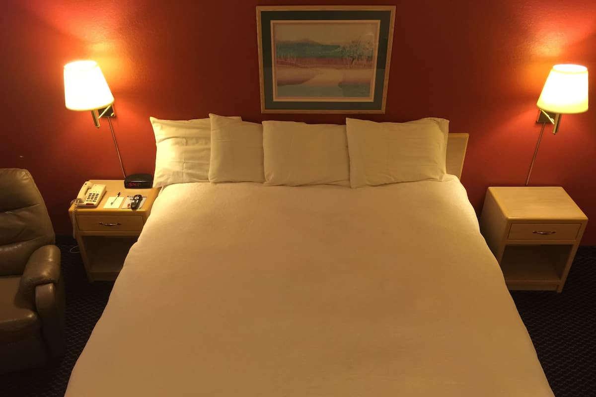 A hotel room with a large bed, two bedside tables, a chair, and a painting on the wall.
