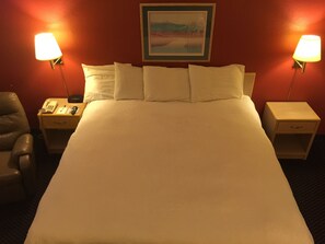 A hotel room with a large bed, two bedside tables, a chair, and a painting on the wall. - Americas Best Value Inn Garden City (Garden City)