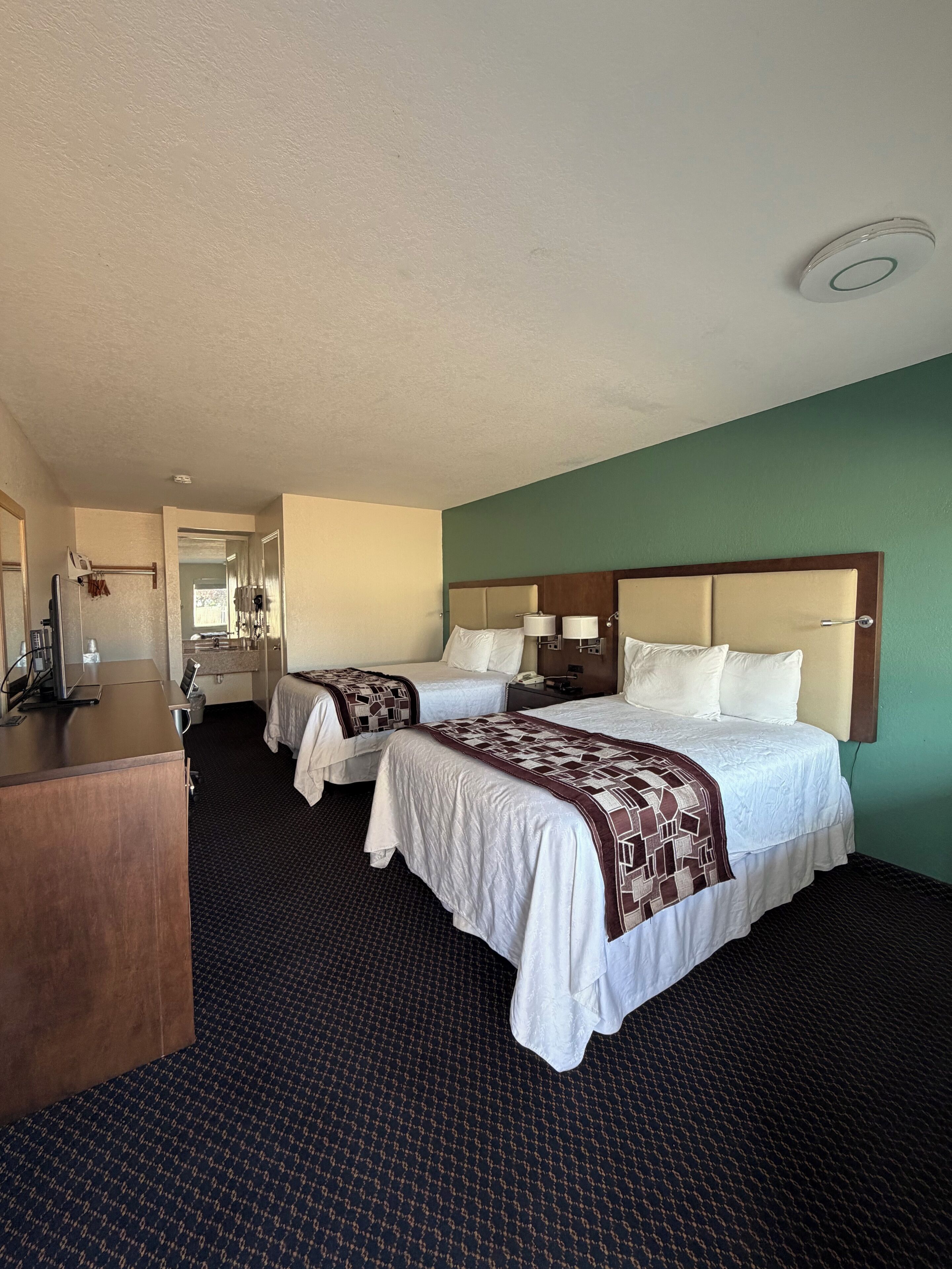 A hotel room with two beds, a desk, and a mirror.