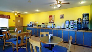 Un restaurante con paredes amarillas, sillas de madera, una barra con una máquina de café y un ventilador de techo.