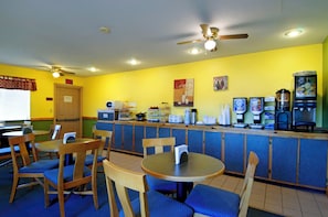 A restaurant with yellow walls, wooden chairs, a counter with a coffee machine, and a ceiling fan. - Americas Best Value Inn Garden City (Garden City)