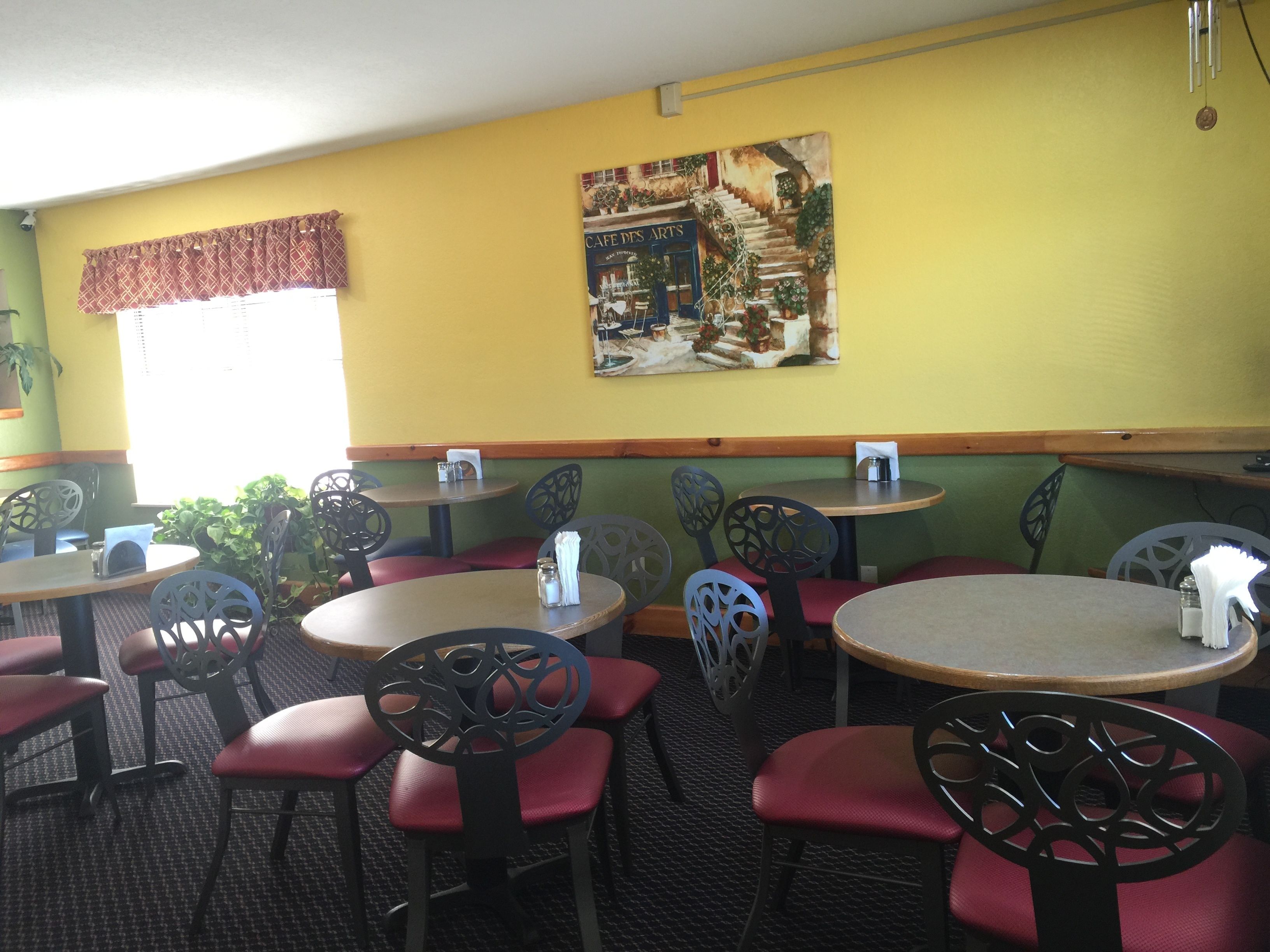 L’intérieur d’un restaurant avec des tables et des chaises rondes, un mur jaune et un tableau représentant un café.