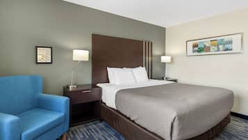 Une chambre d’hôtel avec un grand lit, un fauteuil bleu, une table de chevet avec une lampe et un tableau encadré au mur.