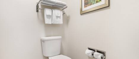 A bathroom with a toilet, a towel rack with towels, and a framed picture on the wall.