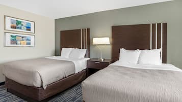 A hotel room with two beds, a nightstand, a lamp, and framed pictures on the wall.